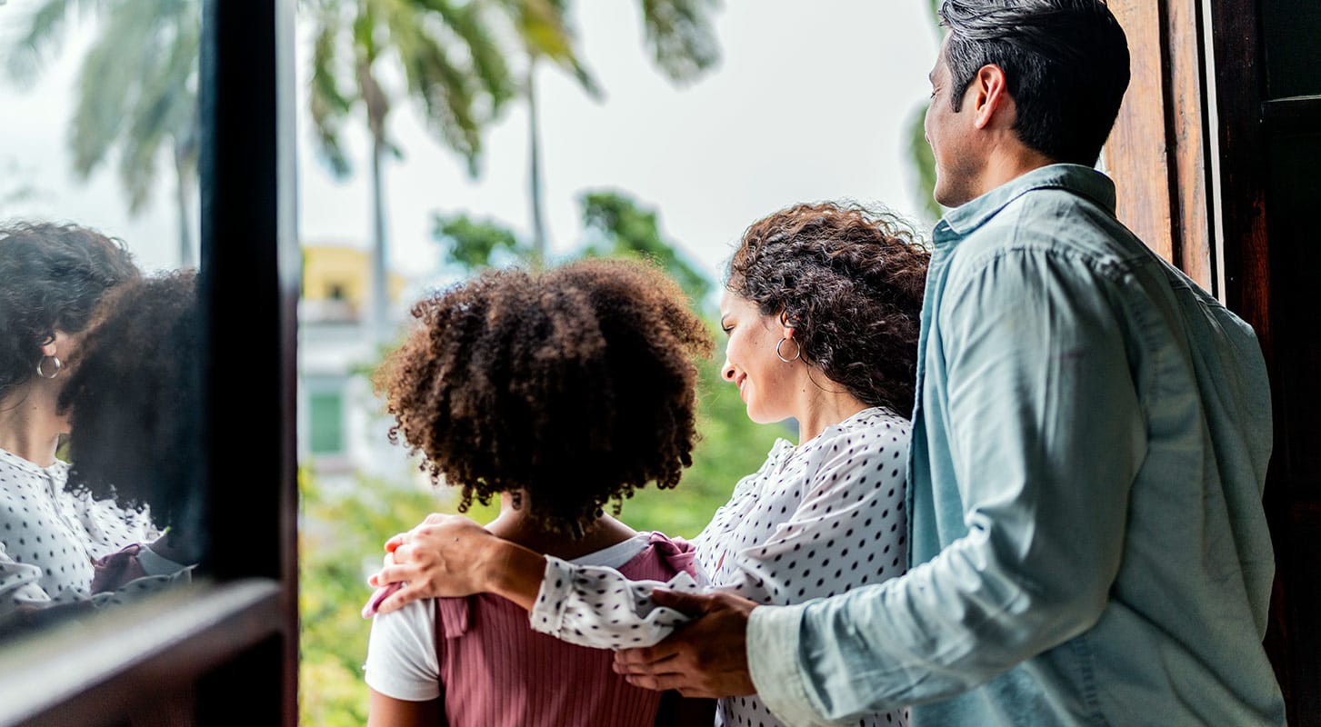 A family gazes out a window, admiring a vibrant tropical landscape filled with lush greenery and bright blue skies.